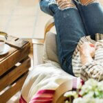 Your Brain Is Not Your Storage Unit (Especially During the Holidays) Person relaxing in a sunlit chair with a book and tea, reflecting a calm and unhurried moment at home.